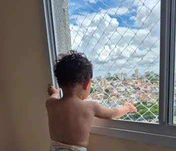 Criança apoiada na janela protegida por rede, em apartamento de São Paulo